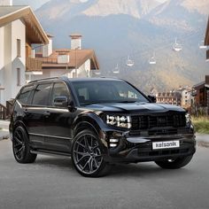 a large black suv parked in front of some houses with mountains in the back ground