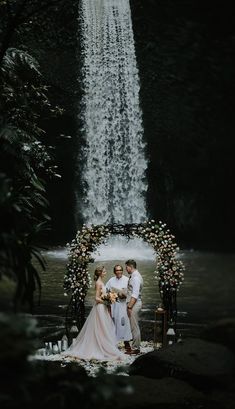 a bride and groom standing in front of a waterfall