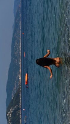 a woman is swimming in the ocean with an orange surfboard on her back and one hand up above her head