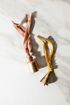 two tassels tied together on a marble counter top, one gold and the other pink