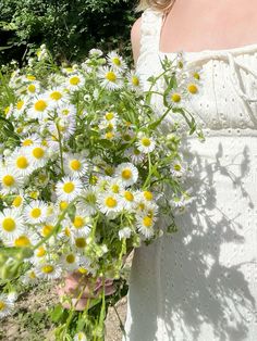 a woman holding a bouquet of daisies in her hand