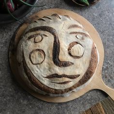 a face made out of bread sitting on top of a wooden board next to a potted plant