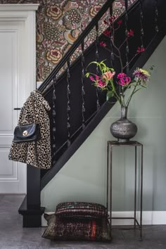 a leopard print coat and vase with flowers on a table in front of a stair case