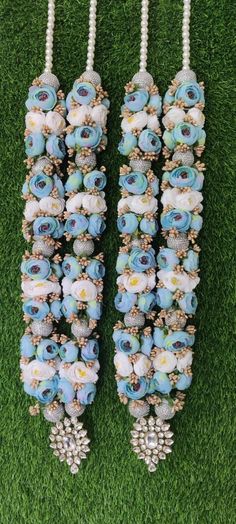 two necklaces made out of blue and white flowers on green grass with pearls hanging from them