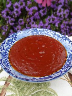 a blue and white bowl filled with sauce on top of a table next to purple flowers