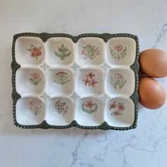 Add vintage style to your kitchen with our Stoneware Egg Tray with Cottage Style. This egg holder is perfect for any farmhouse kitchen. The floral print tray holds a dozen eggs, and is perfect for keeping them close at hand when cooking and baking. It features a dark sage green base with sweet pink cottage flower graphics in each egg cup. This egg holder is also the ideal size  slip into the refrigerator.  Eggs not included. Dishwasher safe. 7.75L x 6W x 1.25H Cute Egg Holder, Cute Baking Supplies, Sage Green Things, Wire Wall Basket, Dark Sage Green, Cottage Apartment, Flower Graphics, Wood Eggs