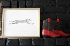 a black and white cheetah print sitting on top of a brick wall next to a pair of red boots