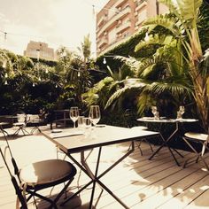 a table and chairs on a wooden deck surrounded by greenery with buildings in the background