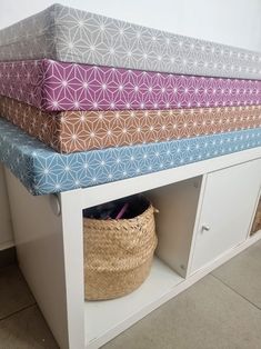 a shelf with several different colored cushions on it and a basket in front of it