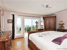 a bedroom with hardwood floors and large windows overlooking the ocean is pictured in this image