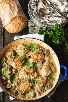 a pot filled with chicken and mushrooms on top of a wooden table next to bread