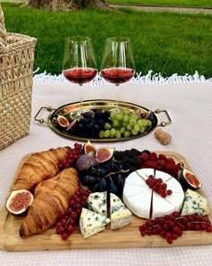 an assortment of cheeses, fruit and bread on a wooden platter with wine glasses in the background