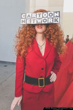 a woman with red hair wearing a red suit and holding a sign over her head