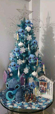 a blue christmas tree decorated with stitchers and snowflakes is on a glass table