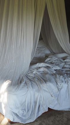 an unmade bed with white drapes on it's headboard and foot board