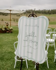 a sign that is sitting in the grass near some chairs and an umbrella with writing on it