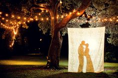 two people standing under a tree with lights