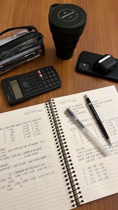 an open notebook sitting on top of a wooden table next to a calculator