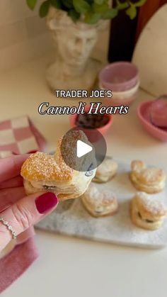 a person holding a pastry in their hand with other pastries on the table behind them