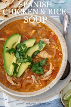 a bowl of chicken and rice soup with avocado on top, next to pita bread