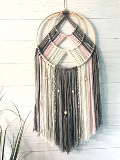 a circular wall hanging with multicolored tassels and beads on a white wood background