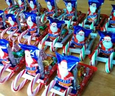 several santa clause toys are lined up on a wooden table with candy bags in the shape of sleighs