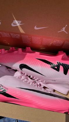 a pair of pink and black nike soccer cleats are in a cardboard box