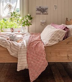 a bed sitting in a bedroom next to a window filled with plants and blankets on top of it