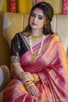 a woman in a pink and black sari sitting on a couch with gold jewelry