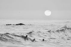 two surfers are riding the waves in front of the sun on a cloudy day