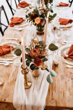 a wooden table topped with lots of plates covered in white and orange napkins next to candles