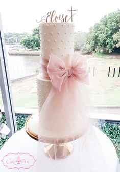 a three tiered wedding cake with pink bow on top sitting in front of a window