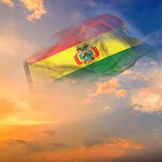 a flag flying high in the sky with clouds around it and sun setting behind it