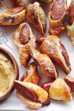 hot dogs and other appetizers on a plate with dipping sauce in a bowl