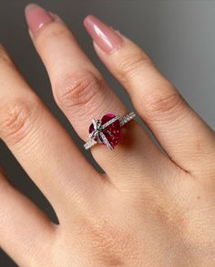 a woman's hand with a diamond and ruby ring on her left hand, in front of a gray background