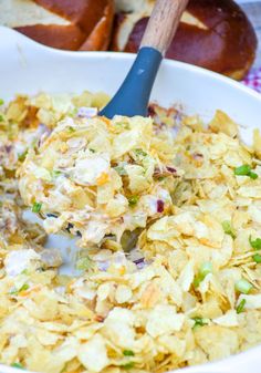 a bowl full of potato salad with a wooden spoon in it and two hot buns in the background