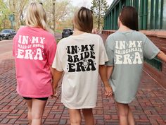 three girls in matching shirts are walking down the brick sidewalk with their arms around each other