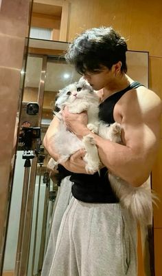 a man holding a cat in his arms while standing next to a mirror and taking a selfie