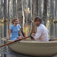 a man and woman are in a boat on the water, with trees around them