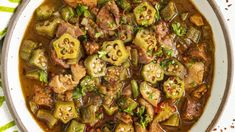 a white bowl filled with meat and vegetables on top of a green table cloth next to a spoon