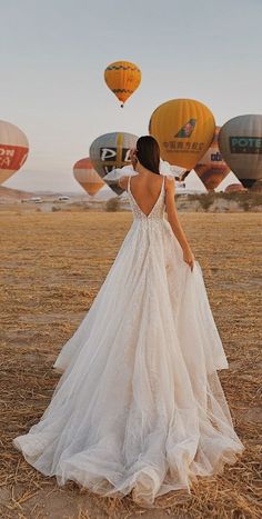 a woman in a white wedding dress looking at hot air balloons