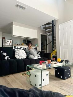 a woman sitting on top of a black couch in a living room next to a stair case