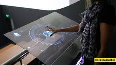 a woman standing in front of a glass table with an electronic device on it's surface