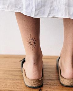 a woman's foot with a small sun tattoo on her left ankle, and a tiny dot in the middle