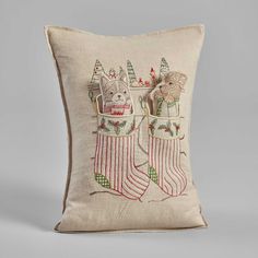 an embroidered pillow with two cats in christmas stockings on the front, and one cat sitting inside