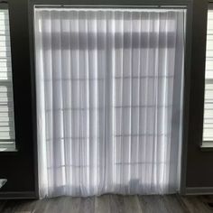 an empty room with two windows and white curtains