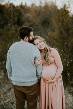 a pregnant couple cuddles in the woods