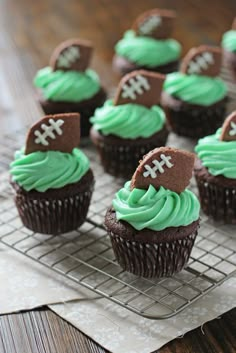 chocolate cupcakes with green frosting and football decorations on a wire cooling rack