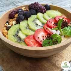 a wooden bowl filled with sliced kiwis, strawberries and other fresh fruit