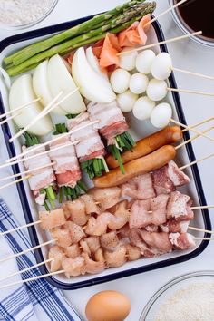 an assortment of meats and vegetables on skewers next to eggs, asparagus, scallions, and other ingredients